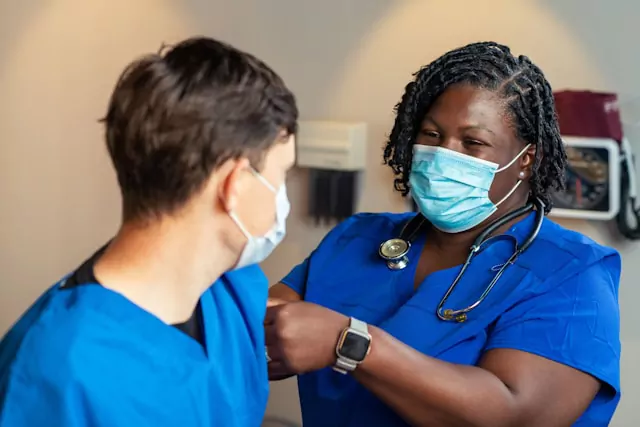 A nurse preceptor in blue scrubs mentoring a nursing student during a clinical demonstration